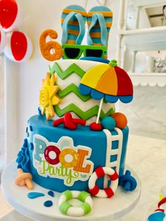 a colorful birthday cake with sunglasses, umbrella and beach balls on the top is sitting on a table