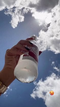 a person is holding up a bottle in the air with clouds behind them and blue sky above