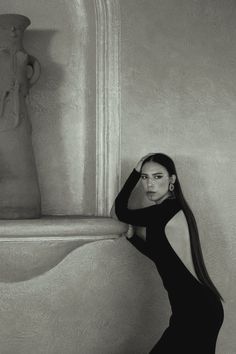 black and white photograph of woman leaning against wall next to vase with statue in background