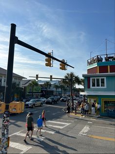 people crossing the street at an intersection with traffic lights and buildings in the background on a sunny day