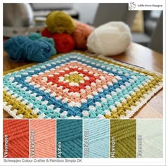 there is a crochet granny blanket on the table with balls of yarn next to it