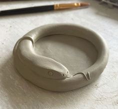 a ceramic snake ring sitting on top of a table next to a pen and pencil