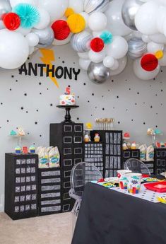 a birthday party with balloons and decorations on the wall, including a black table cloth