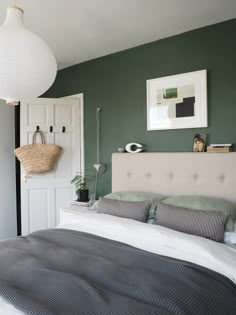 a bedroom with green walls and white bedding in the center is a basket hanging on the wall