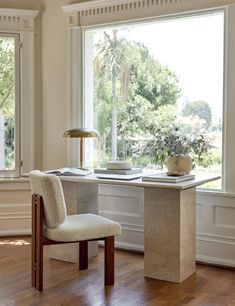 a desk with a chair next to it in front of a window and a potted plant