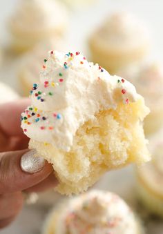 someone holding up a half eaten cupcake with white frosting and sprinkles