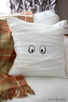 a white pillow with eyes drawn on it sitting on a couch next to plaid throw pillows