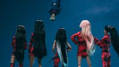 several dolls with long hair standing in front of a group of people wearing red dresses