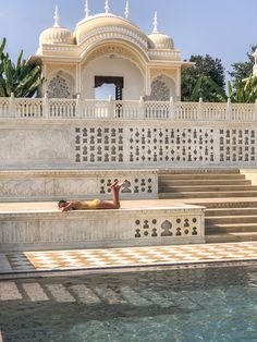 a man laying on top of a stone bench next to a swimming pool in front of a white building