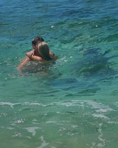 two people swimming in the ocean with their backs to each other and looking at something