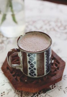 a cup of hot chocolate sitting on top of a wooden tray next to a vase