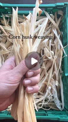 a hand holding a piece of corn husk weaving in front of a green box