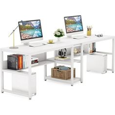 two computer monitors sitting on top of a white desk next to books and other items