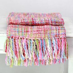 a multicolored blanket sitting on top of a wooden bench next to a white wall