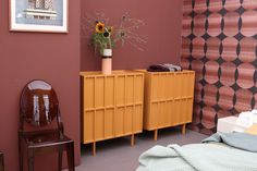 a room with a bed, chair and vase on the dresser next to wall paper