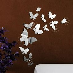 a bunch of butterflies are flying in the air on a brown wall next to a vase with purple flowers