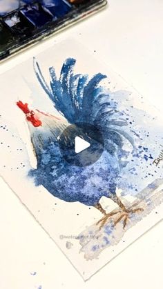 a painting of a blue bird on a white table next to a brush and watercolor palette