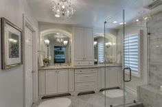 a large bathroom with white cabinets and marble counter tops, chandelier above the tub