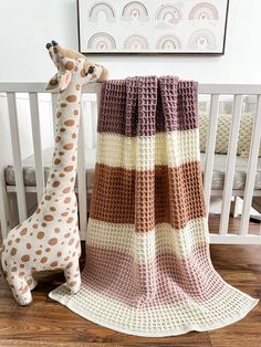 a crocheted giraffe sitting next to a blanket on the floor in a nursery