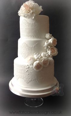 a three tiered wedding cake with white flowers on the top and bottom layer is decorated in lace