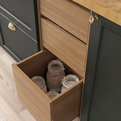 an open drawer with jars in it on top of a wooden floor next to cabinets