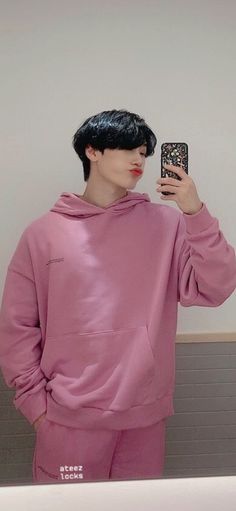 a male in a pink hoodie is taking a selfie with his cell phone