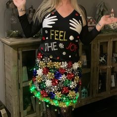 a woman wearing a christmas sweater and skirt with lights on her feet is standing in front of a table