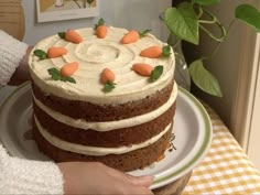 a person is holding a cake with frosting and carrots on it, in front of a potted plant