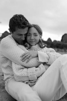 a man and woman sitting on the beach hugging each other, black and white photograph