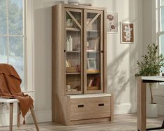 a wooden cabinet sitting next to a window in a room with a chair and table