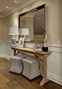 a wooden table topped with two stools next to a large mirror and pictures on the wall