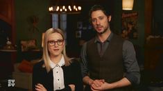 a man and woman standing next to each other in front of a living room filled with furniture