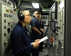 three men in navy uniforms are looking at something while wearing headphones and ear phones