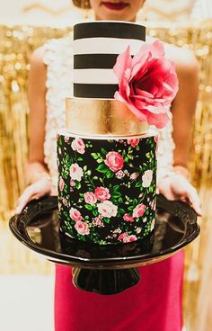 a woman holding a cake decorated with flowers and black and white striped frosting on it