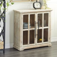 a white wooden cabinet with glass doors and shelves in front of a clock on the wall