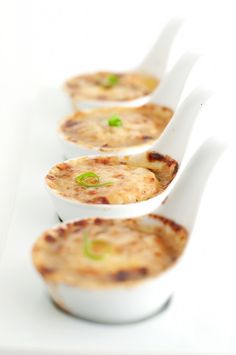 four white spoons filled with food on top of a table next to each other