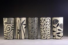 four vases are lined up in a row on a table with black and white designs