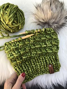 a hand holding a green knitted purse next to a ball of yarn