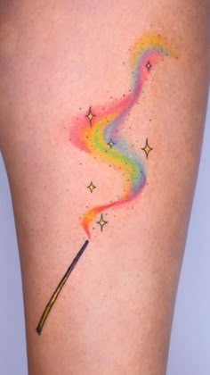 a woman's thigh with a rainbow colored tattoo on her leg and a wand sticking out of it