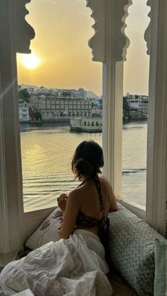 a woman sitting on top of a bed in front of a window next to the ocean