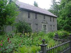 an old house in the woods with lots of greenery around it and a fence