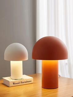 two lamps sitting on top of a wooden table next to a book and lamp shade