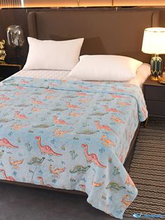 a bed with a blue bedspread covered in pink and orange dinosaurs on it