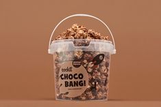 a plastic container filled with chocolate covered granola on top of a brown table next to a wall