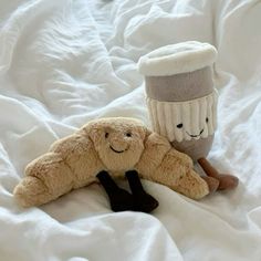 two stuffed animals laying on top of a bed next to a coffee cup and sock