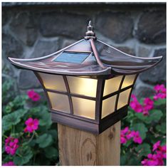 a light that is on top of a wooden post in front of some pink flowers