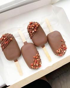 four chocolate covered pops sitting on top of a white box