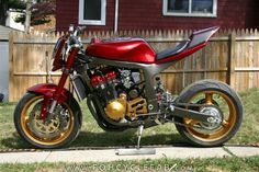 a red motorcycle parked on top of a sidewalk next to a wooden fence in front of a house