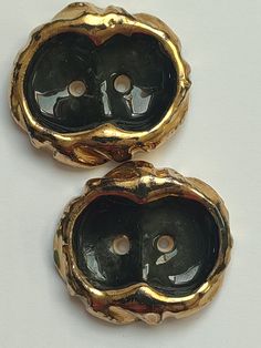 two black and gold buttons with holes in the middle on a white surface, one has an open mouth