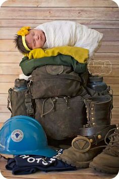 a baby laying on top of a pile of luggage next to a blue hard hat